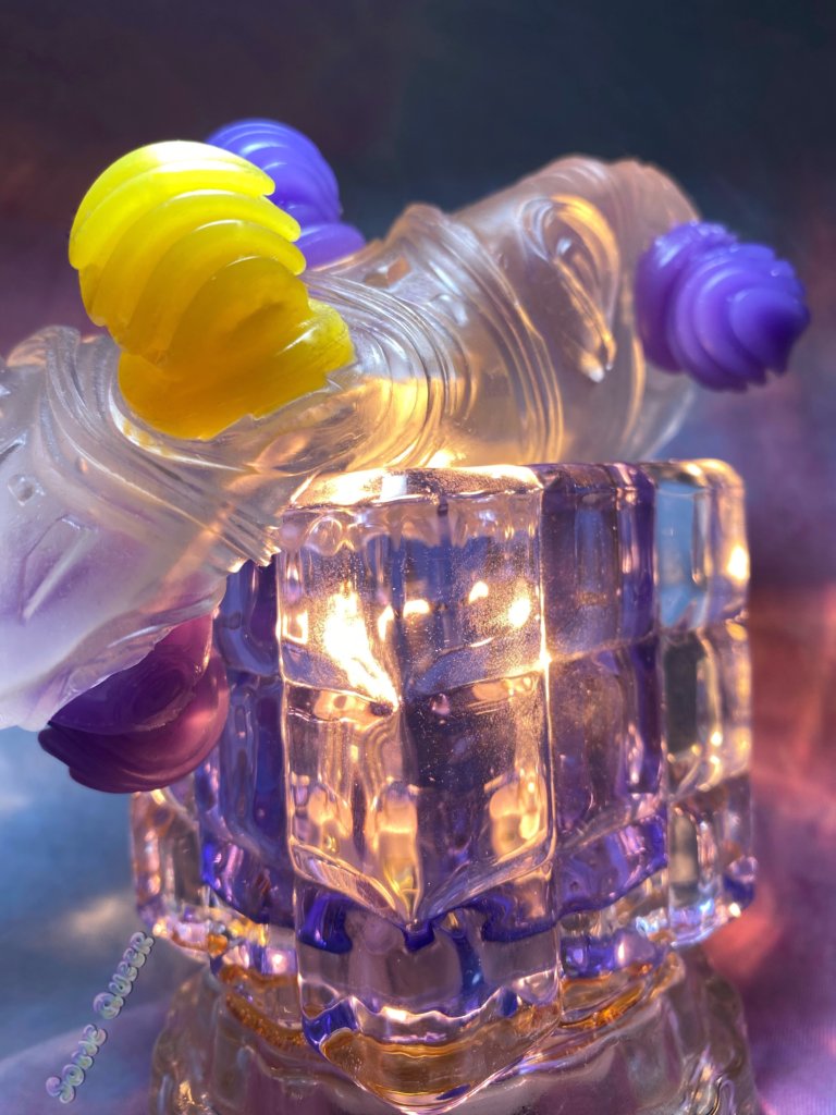 Tenga Bobble Magic Marbles inverted, propped on top of a cube shaped crystal light. The stroker is clear T.P.E with yellow and purple orbs